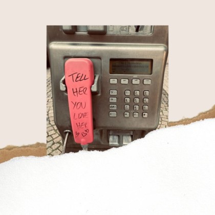 Eine Telefonzelle. Auf dem Hörer steht: Tell her you love her