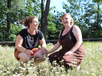 Isa und Anna knien in einer Blumenwiese und lachen